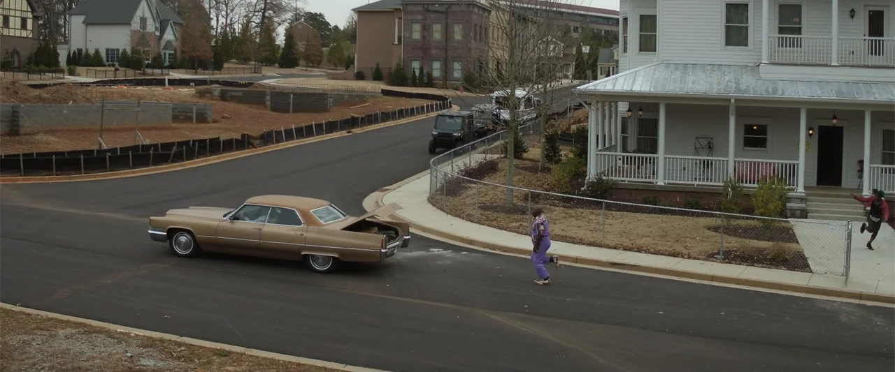 Maxine's Baby: The Tyler Perry Story (2023) movie still: wide — A suburban residential street features new house construction and a beige vintage…