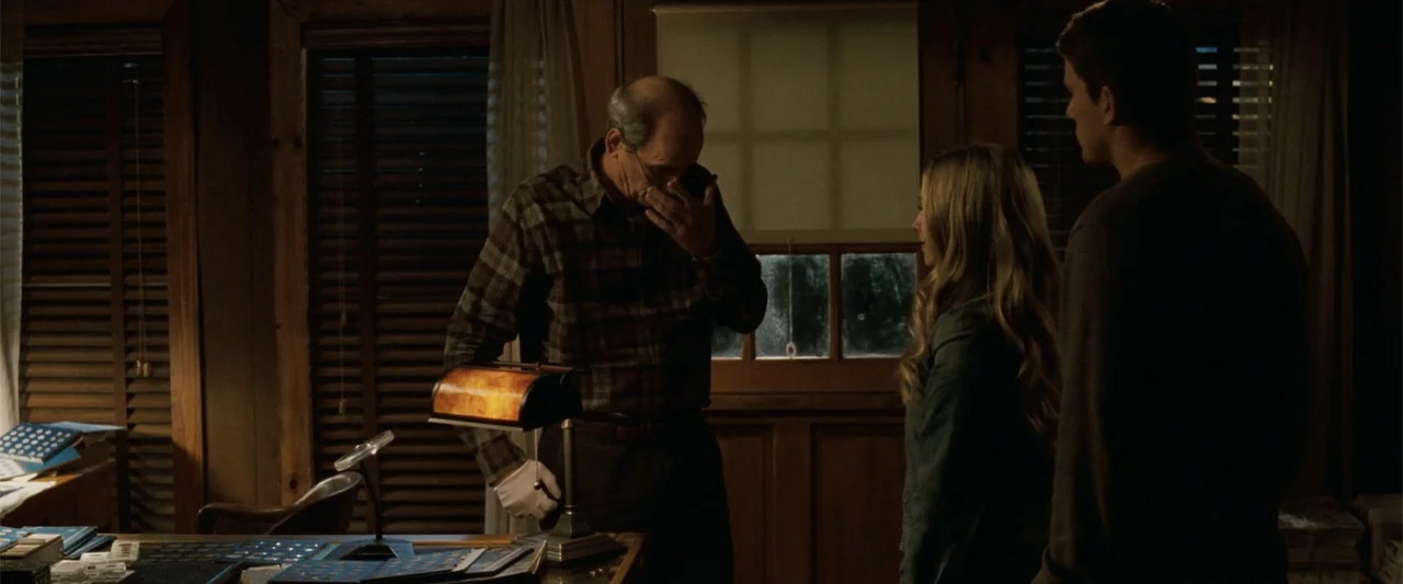 Dear John (2010) movie still: medium — A dimly lit room features wood-paneled walls and a desk cluttered with coin collectors supplies. An older man…
