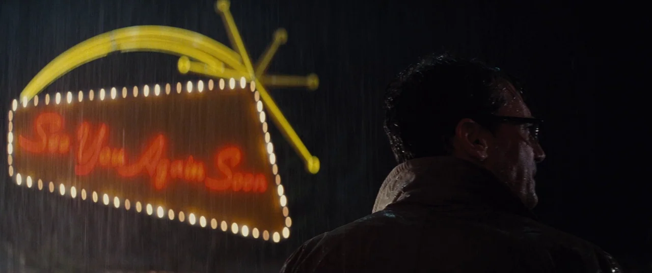Bad Times at the El Royale (2018) movie still: medium — A man stands in the rain at night before a large mid-century neon sign. The sign glows in…