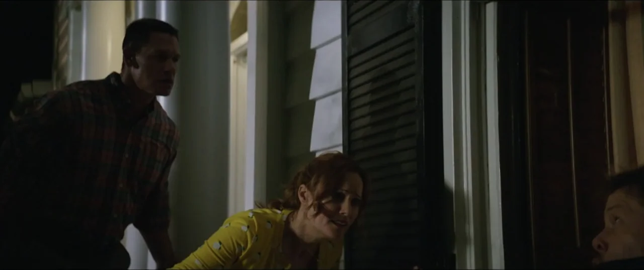 Blockers (2018) movie still: medium — A dark porch with white wooden siding and dark shutters at night. Two people stand together looking towards…