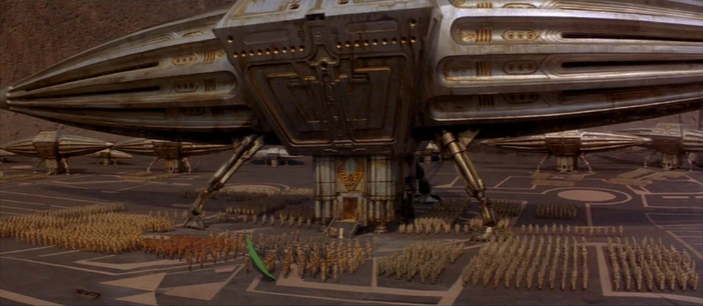 Dune (1984) movie still: wide — A vast, barren landscape holds several colossal, metallic, spindle-shaped spacecraft resting on landing gear.…