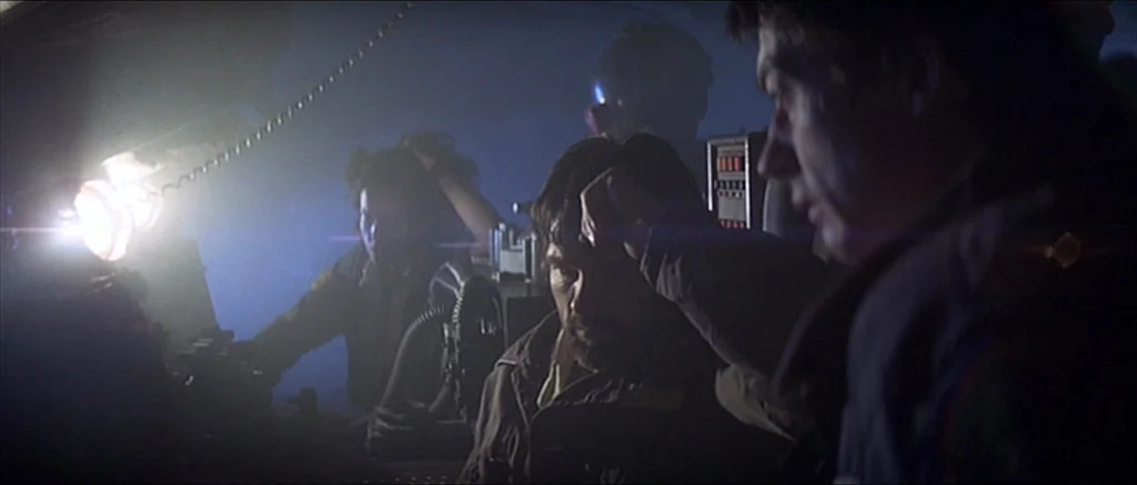 Alien (1979) movie still: medium — A dark, cramped technological control room with glowing consoles and metallic machinery elements. Multiple people…