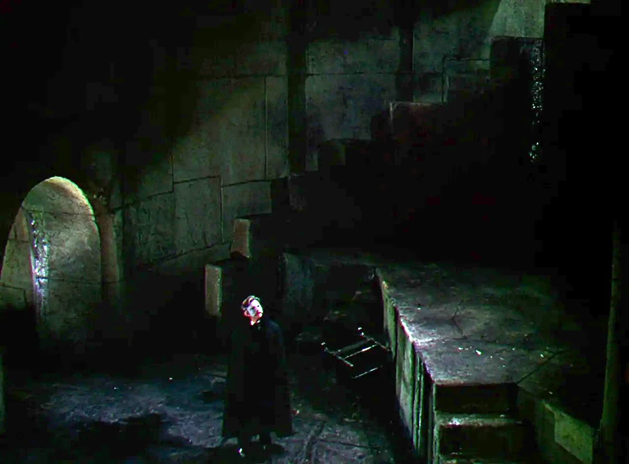 Phantom of the Opera (1943) movie still: wide — A dark subterranean chamber features textured stone blocks and a shadowed arched doorway nearby. A…