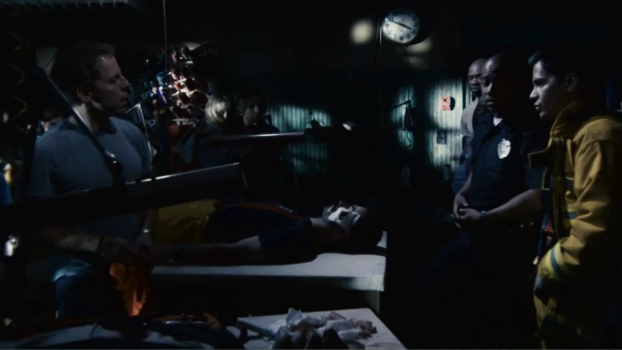 Quarantine (2008) movie still: medium — A dimly lit room contains medical supplies and a man lying on a cot. Several figures in uniform stand near…