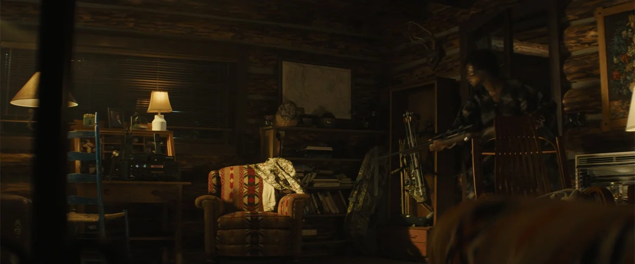 Those Who Wish Me Dead (2021) movie still: medium — A dark log cabin interior features wooden walls and shelves filled with various items. A person…