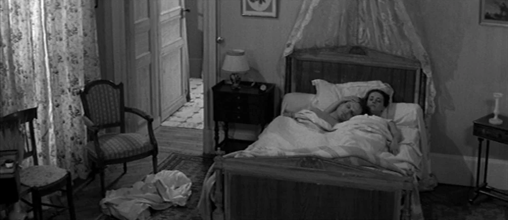Les Amants (1958) movie still: wide — A furnished bedroom features a large bed with a canopy and floral curtains. A man and woman lie side by side…