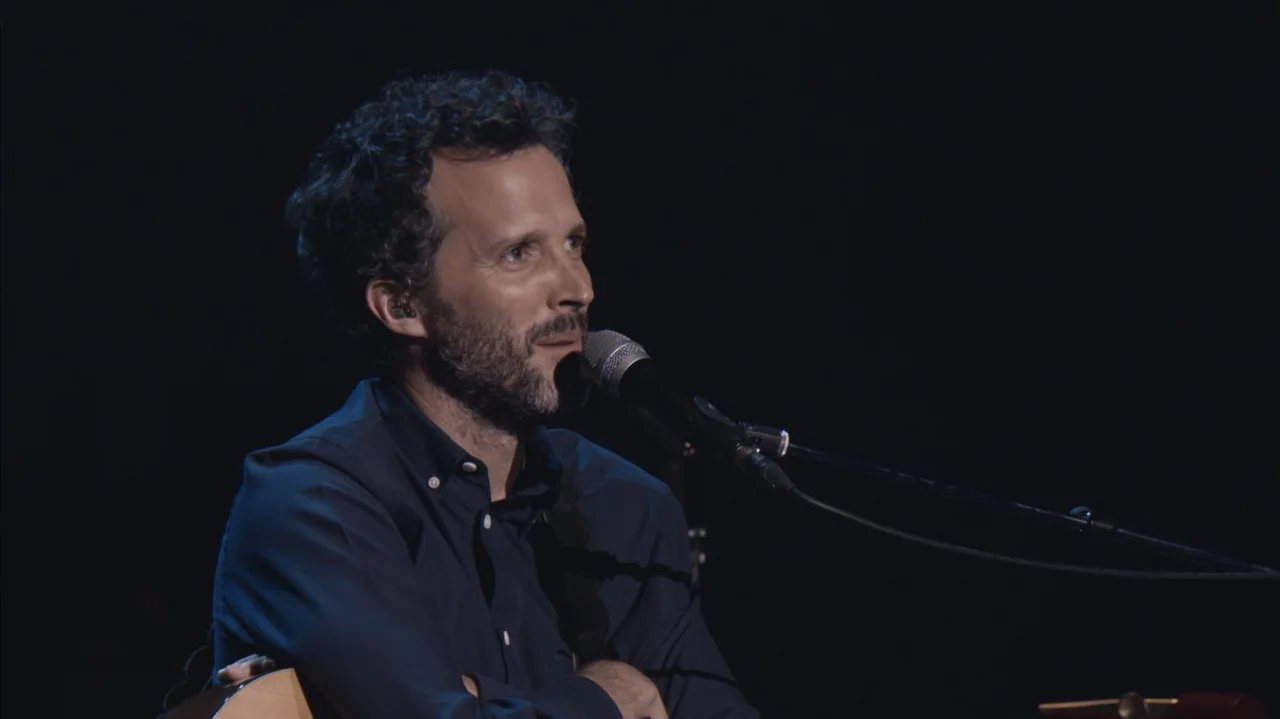 Flight of the Conchords: Live in London (2018) movie still: medium — A dark concert stage with a performer illuminated by a single light source. A…