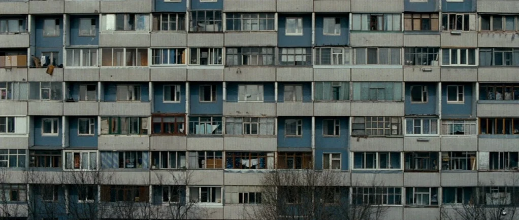 Elena (2011) movie still: establishing — A massive, repetitive concrete apartment building with many rows of windows and balconies. The facade shows…