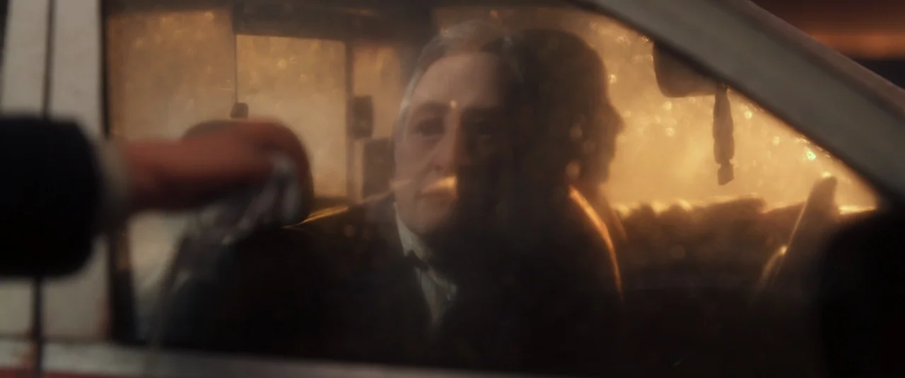 Anomalisa (2015) movie still: medium — The interior of a car at night is lit by ambient yellow street light. An older man sits in the driver's seat…