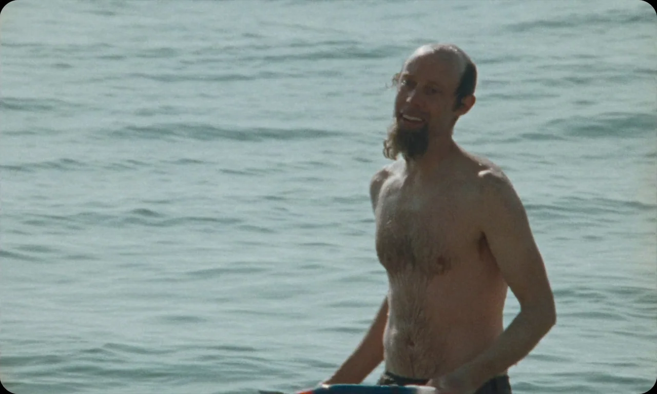 Vulcanizadora (2024) movie still: medium — A man stands waist-deep in open water under natural daylight. He smiles toward the camera with his chest…