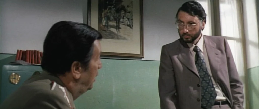 Don’t Torture A Duckling (1972) movie still: medium — An interior office space with sage green walls and a framed print. A man in a suit faces a…