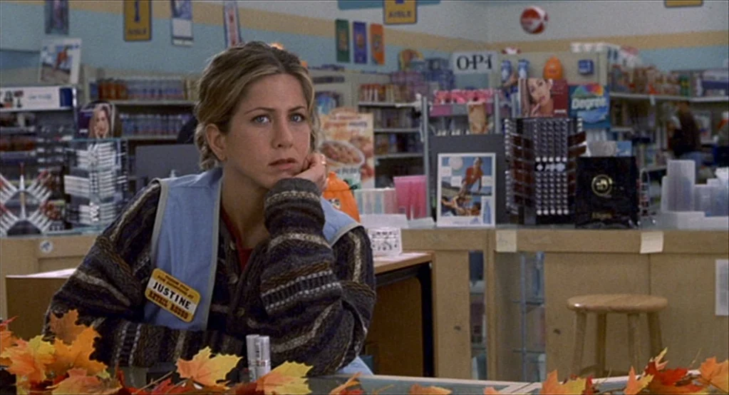 The Good Girl (2002) movie still: medium — A retail interior features shelves filled with various beauty and household products. A woman in a retail…
