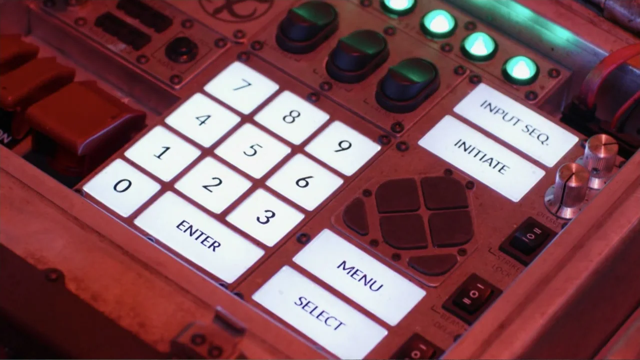 Mortal Engines (2018) movie still: closeup — A close-up of a metallic control panel featuring a backlit numerical keypad and buttons. The console…