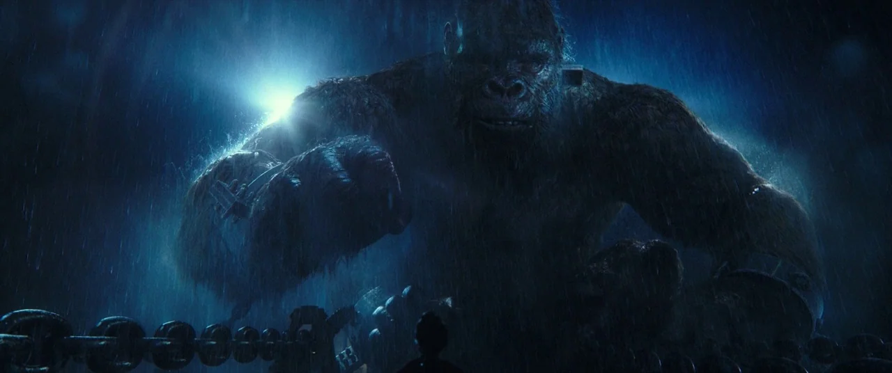 Godzilla Vs. Kong (2021) movie still: medium — A massive gorilla stands in the rain at night on the open ocean surface. It holds a large metal chain…