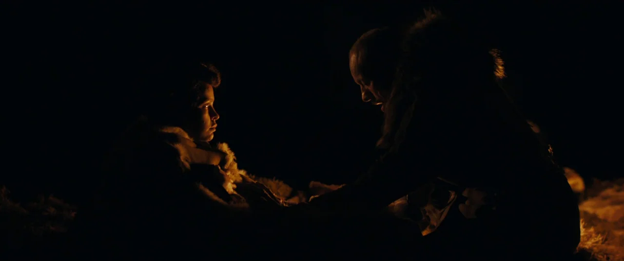Out of Darkness (2022) movie still: medium — A dark, unidentifiable outdoor area at night illuminated by a nearby campfire. An adult man wearing…