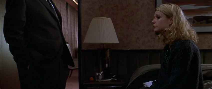 Hard Eight (1996) movie still: medium — A dimly lit room with brown wallpaper and a table lamp on a nightstand. A woman sits on a bed facing a man…