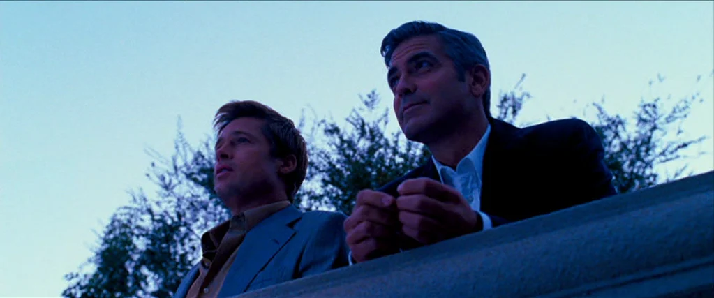 Ocean’s Thirteen (2007) movie still: medium — Two men stand on a balcony overlooking trees during the blue hour. They lean on a stone railing while…