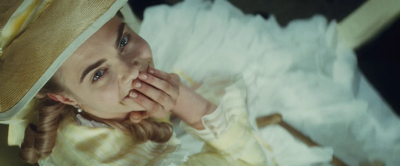 Anna Karenina (2012) movie still: closeup — A woman sits inside an open carriage wearing a period-appropriate hat and dress. She looks upward at the…