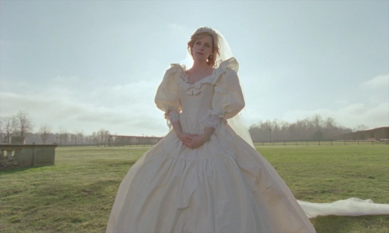 Spencer (2021) movie still: fullbody — A woman in a voluminous wedding dress stands alone in an expansive grassy field. She looks upward while…