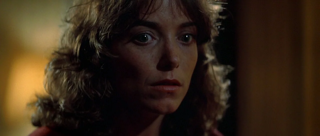 Starman (1984) movie still: closeup — A dimly lit interior room serves as the setting for a portrait shot. A woman with wavy brown hair looks…