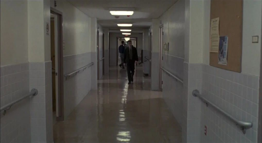 Light Sleeper (1992) movie still: wide — A long hospital corridor features white tile walls and gray wainscoting with handrails. A man walks toward…