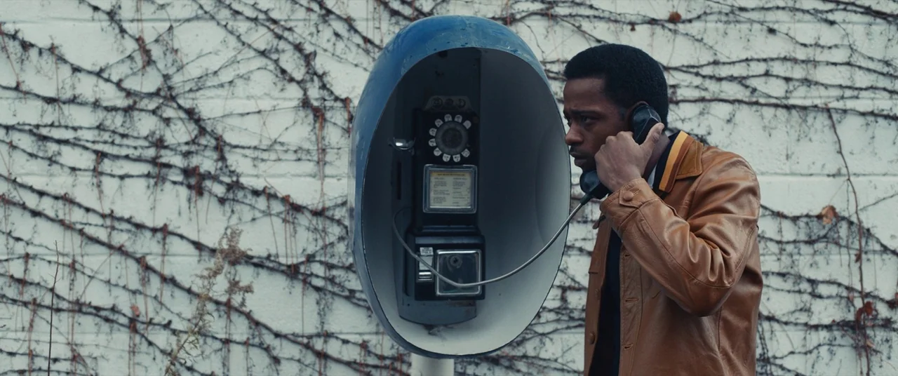 Judas and the Black Messiah (2021) movie still: medium — An outdoor area with a white cinderblock wall covered in dried climbing vines. A man in a…