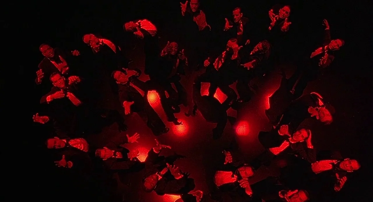 Chicago (2002) movie still: wide — A dark performance space is illuminated by bright red spotlights arranged in a circle. Multiple men in black…