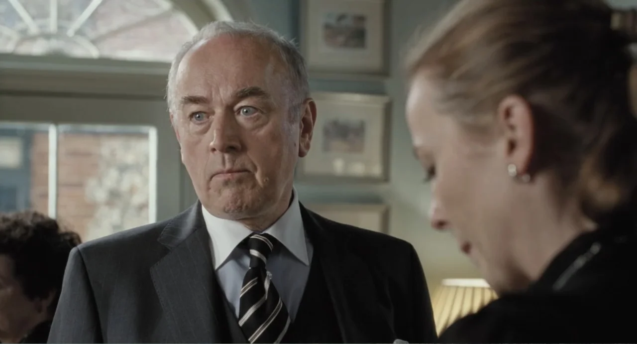 Death at a Funeral (2010) movie still: medium — An interior domestic space features framed art on the wall and a bright window. An older man in a…