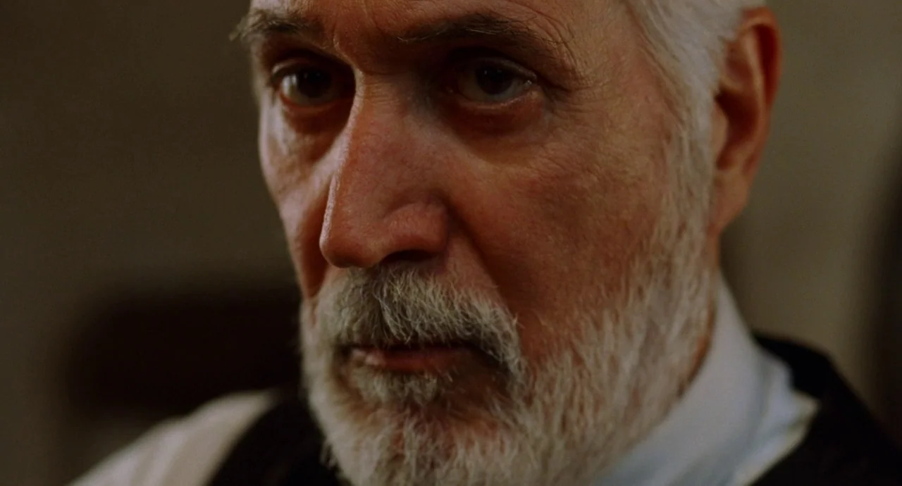 The Devils Backbone (2001) movie still: closeup — A close-up view of an elderly man with a gray beard and white hair. The man faces the camera while…