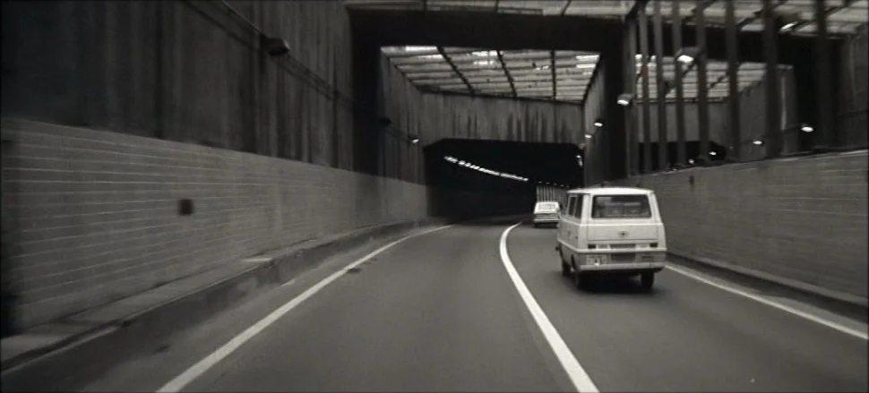 Solaris (1972) movie still: wide — An open highway tunnel with concrete walls and periodic overhead lighting supports. Two boxy vans travel along…