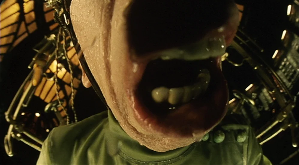 The City Of Lost Children movie still: closeup — A man's face is shown in extreme closeup inside a dark mechanical setting. He is screaming while…
