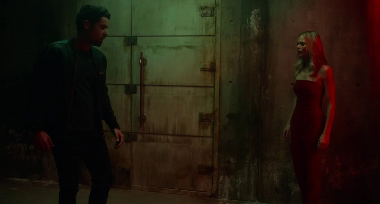 Rabid (2019) movie still: fullbody — A man and a woman stand on opposite sides of a large metal doorway. The room is constructed of dark, stained…