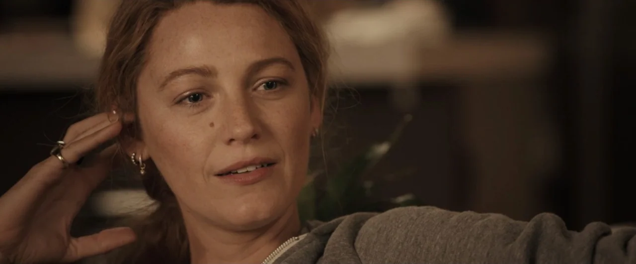 It Ends with Us (2024) movie still: closeup — An interior living room with muted, neutral-toned walls and soft ambient lighting. A woman in a gray…