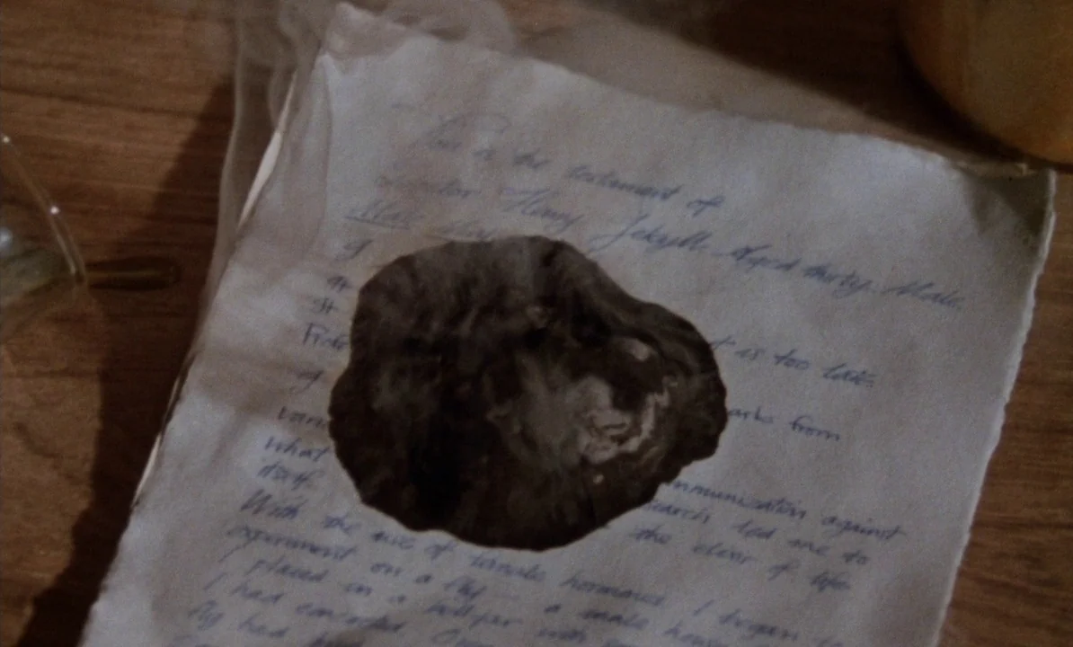 Dr Jekyll & Sister Hyde (1971) movie still: closeup — A cream-colored sheet of handwritten parchment rests on a wooden surface. A large, dark…