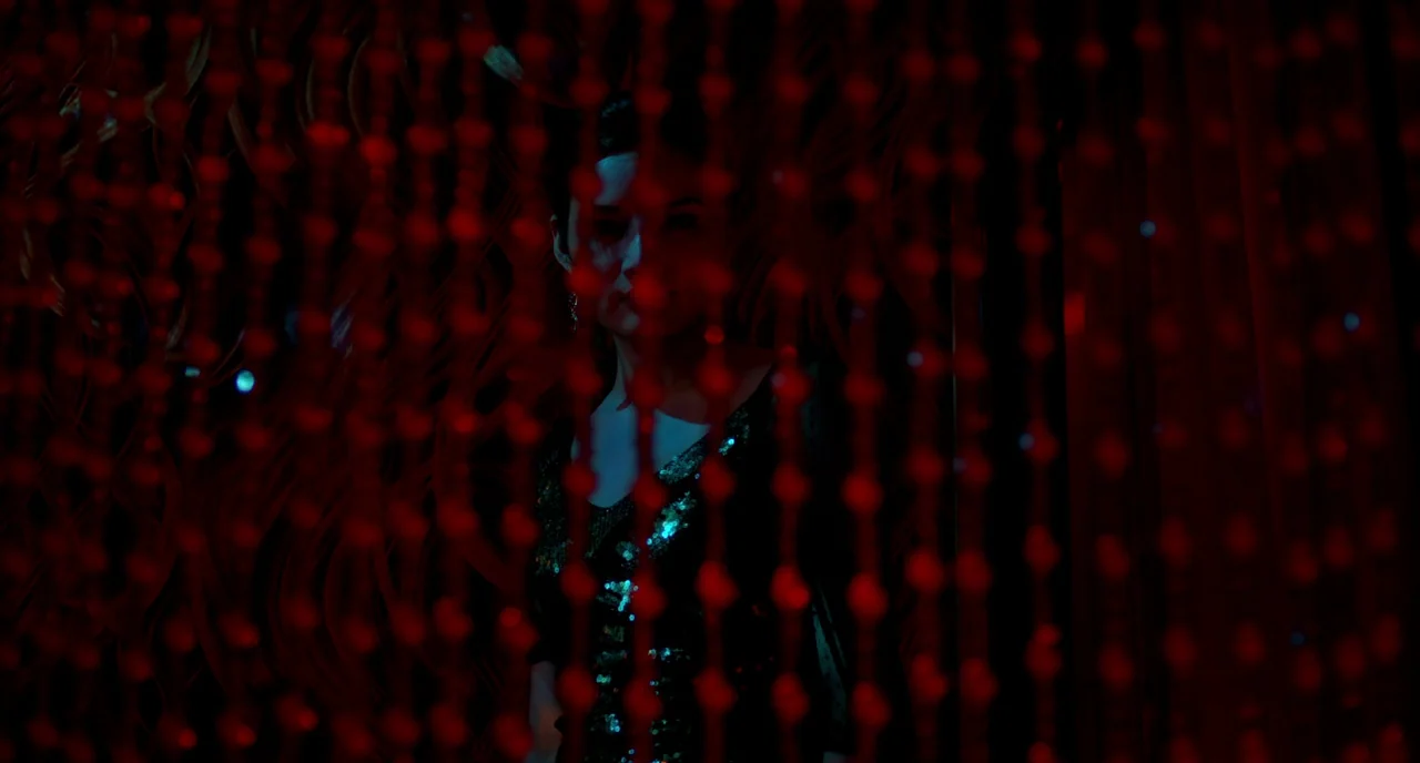 Only God Forgives (2013) movie still: medium — A dark space obscured by vertical red beaded curtains that act as a foreground layer. A woman with…