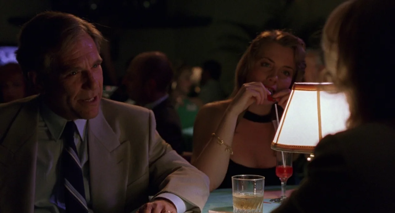 To Die For (1995) movie still: medium — A dimly lit restaurant table is illuminated by a small lamp with a fabric shade. A man in a suit and a woman…