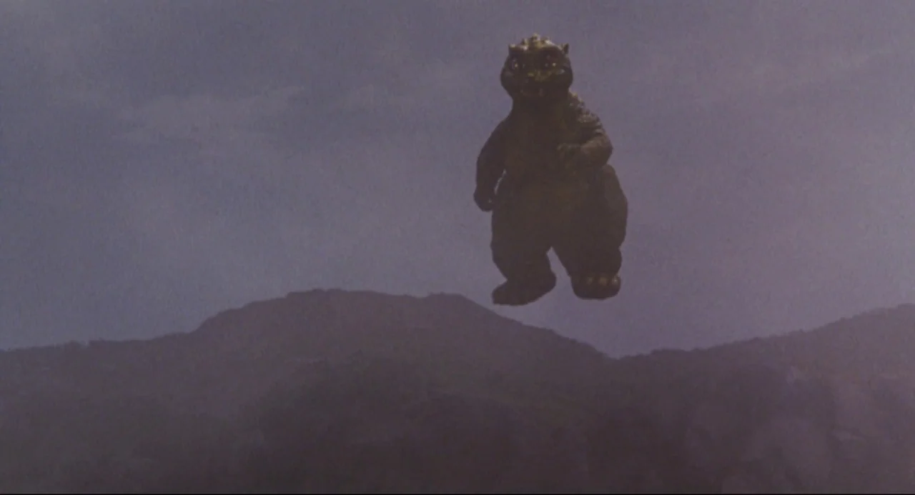 Godzilla vs. SpaceGodzilla (1994) movie still: wide — A vast overcast sky hangs over dark, rolling mountain ridges. A bipedal reptilian monster…