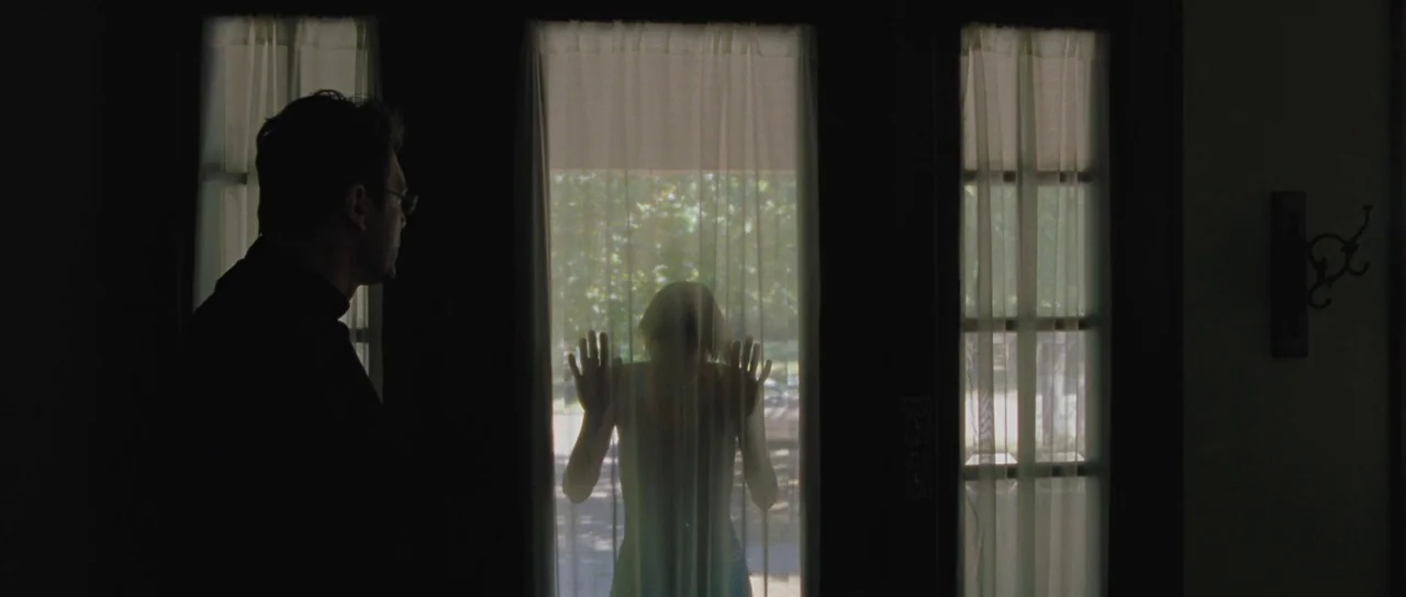 To The Wonder (2012) movie still: medium — A dimly lit interior room featuring a glass front door with white curtains. A man stands on the left…