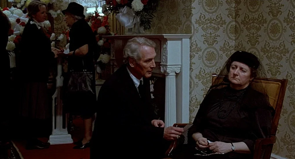 The Verdict (1982) movie still: medium — A room with patterned wallpaper and large floral arrangements stands behind the subjects. An older man in a…
