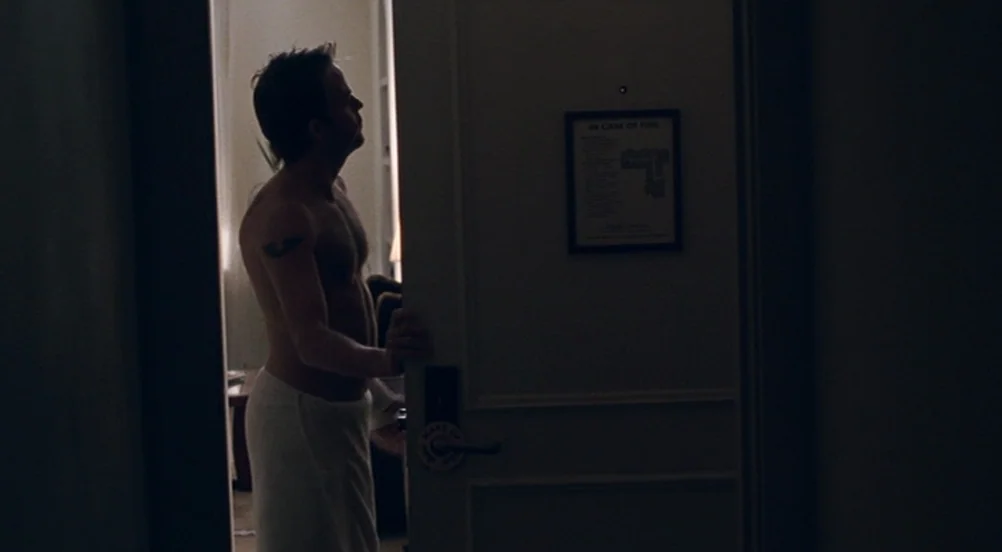 Somewhere (2010) movie still: medium — A dark hallway leads to an illuminated space through an open door. The man stands in the doorway looking into…