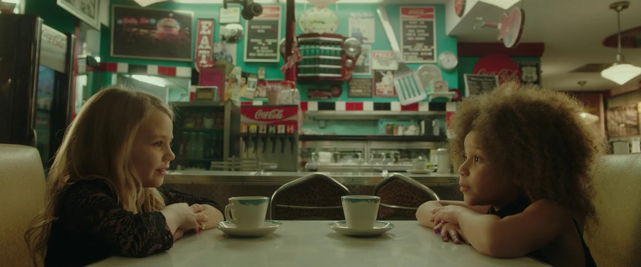 Spontaneous (2020) movie still: medium — A diner booth decorated with vintage Coca-Cola memorabilia and a turquoise-painted wall. Two young girls…