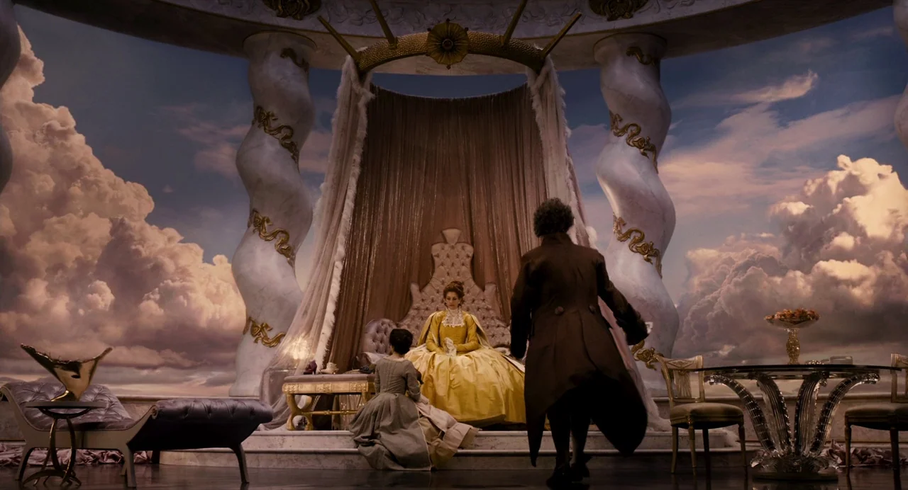 Mirror Mirror (2012) movie still: wide — A lavish royal chamber features large marble pillars and a painted sky backdrop. A queen in a yellow dress…