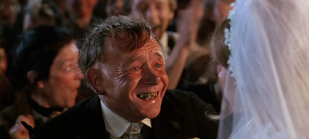 Ryan’s Daughter (1970) movie still: closeup — An older man with deep facial lines smiles widely at a woman wearing a veil. A crowded, out-of-focus…