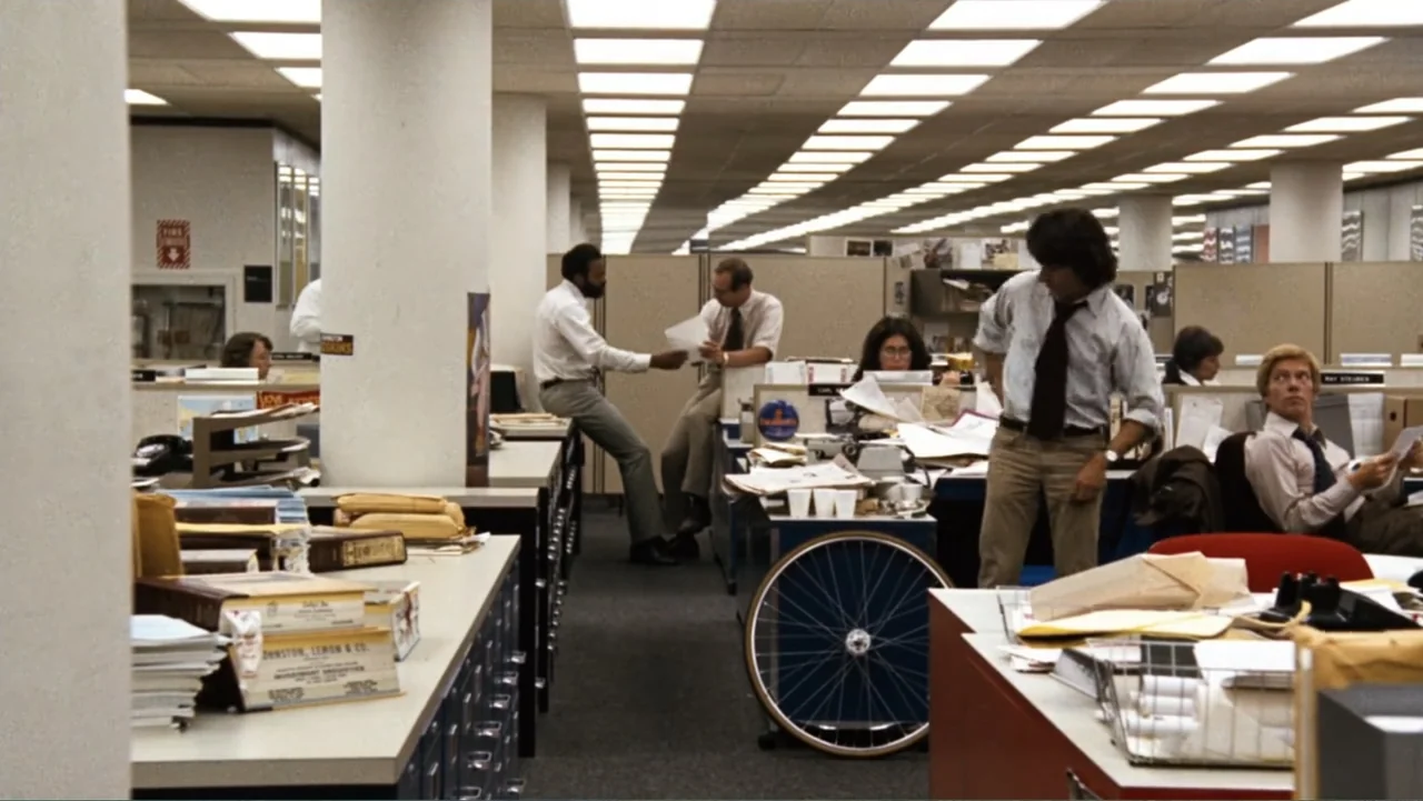 All the President's Men (1976) movie still: wide — A busy 1980s corporate workspace with rows of cubicles and scattered paperwork everywhere.…