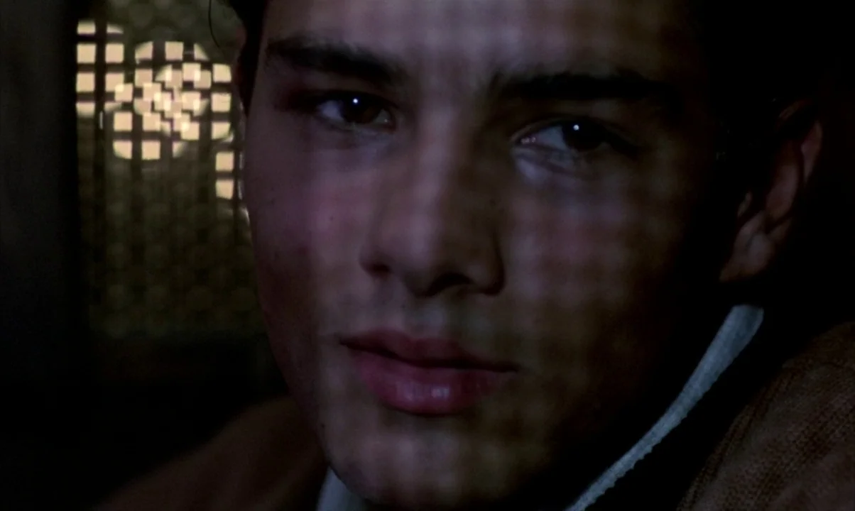 Cinema Paradiso (1988) movie still: closeup — The face of a young man is partially obscured by a geometric shadow pattern. He stares directly at the…