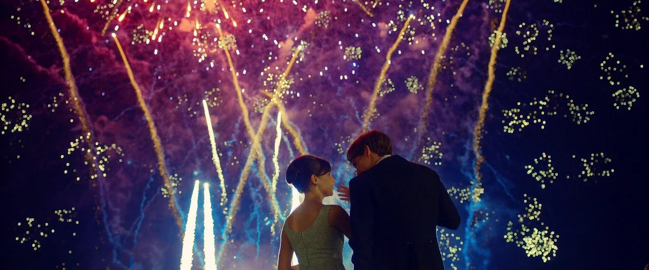 The Theory of Everything (2014) movie still: fullbody — A pair of people stand beneath a dark night sky filled with bright fireworks. The…