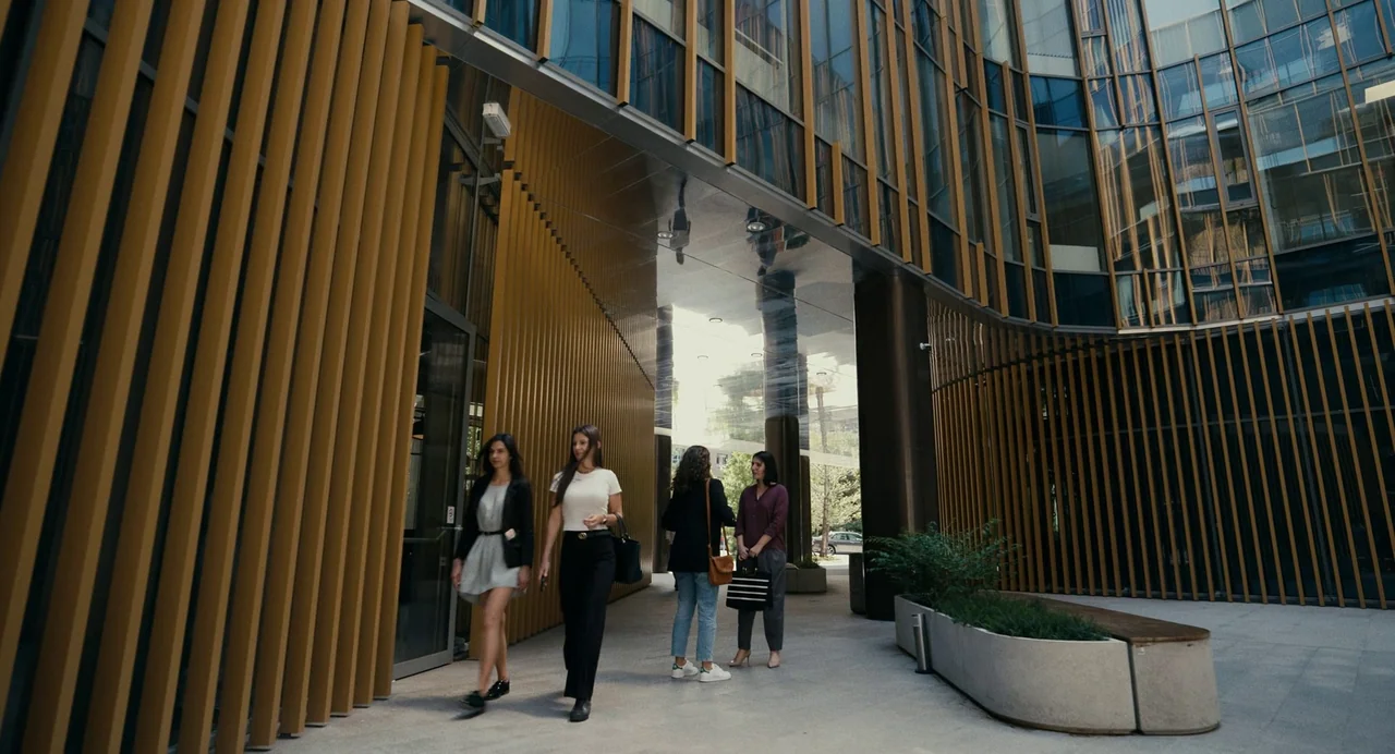 Barbarian (2022) movie still: fullbody — A modern commercial courtyard features floor-to-ceiling glass windows and vertical wooden decorative slats.…