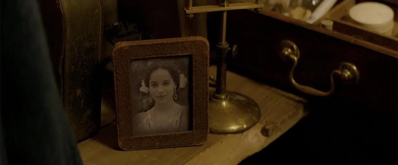 Fantastic Beasts and Where to Find Them (2016) movie still: closeup — A close-up shot focuses on a small framed photograph on a wooden table. The…