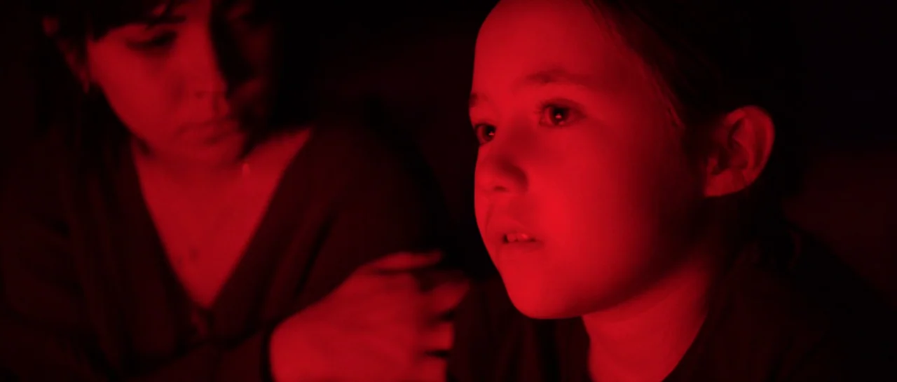 The Boogeyman (2023) movie still: medium — A dimly lit room filled with deep shadows and red lighting. A young child stares off-screen while an…