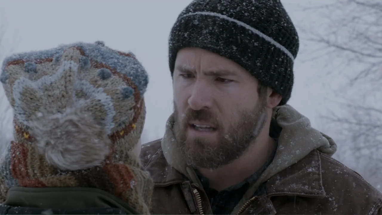 The Captive (2014) movie still: medium — A snowy outdoor landscape with blurred trees in the background under an overcast sky. A man in a winter hat…